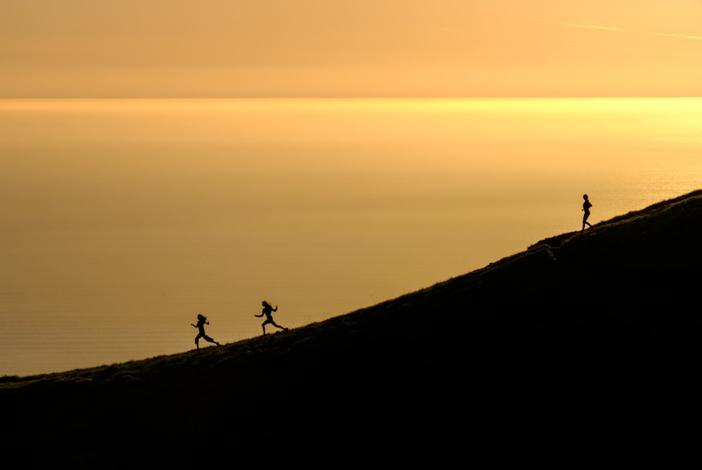 three persons running downhill during golden hour