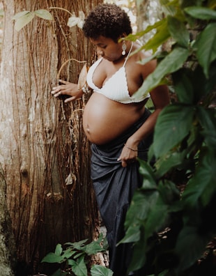 a pregnant woman leaning against a tree in a forest
