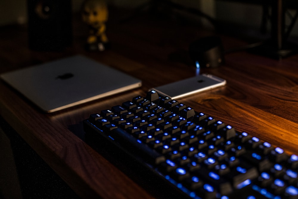 A dim picture of a blue backlit keyboard, a smartphone and a tablet on a wooden desktop