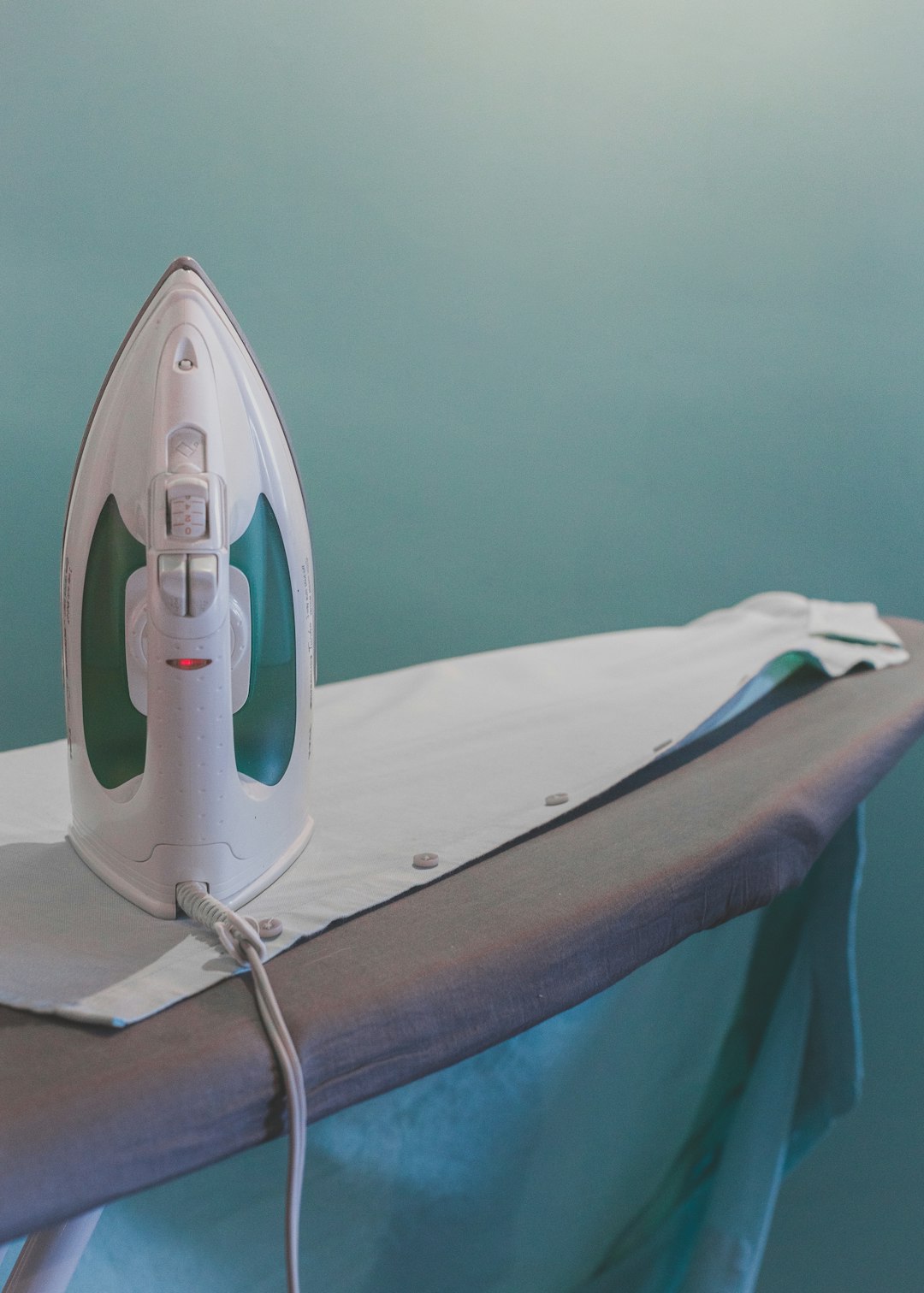  white and teal steam clothes iron plugged on ironing board ironing board