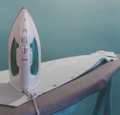 white and teal steam clothes iron plugged on ironing board