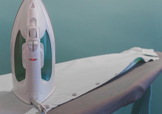 white and teal steam clothes iron plugged on ironing board