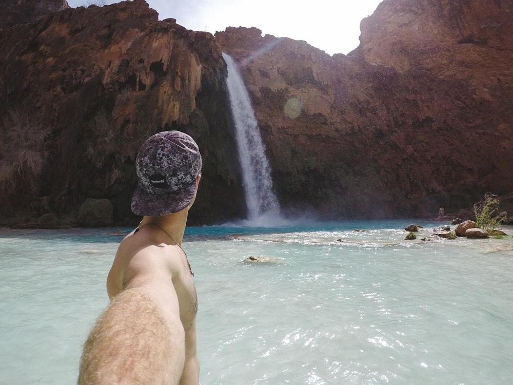 Homme au bonnet noir assis sur un rocher devant des cascades pendant la journée