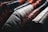 A close-up view of several leather jackets hanging on a rack, showcasing different colors such as black, red, white, and brown. The texture of the leather is highlighted, with visible stitching and wear.