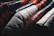 A close-up view of several leather jackets hanging on a rack, showcasing different colors such as black, red, white, and brown. The texture of the leather is highlighted, with visible stitching and wear.