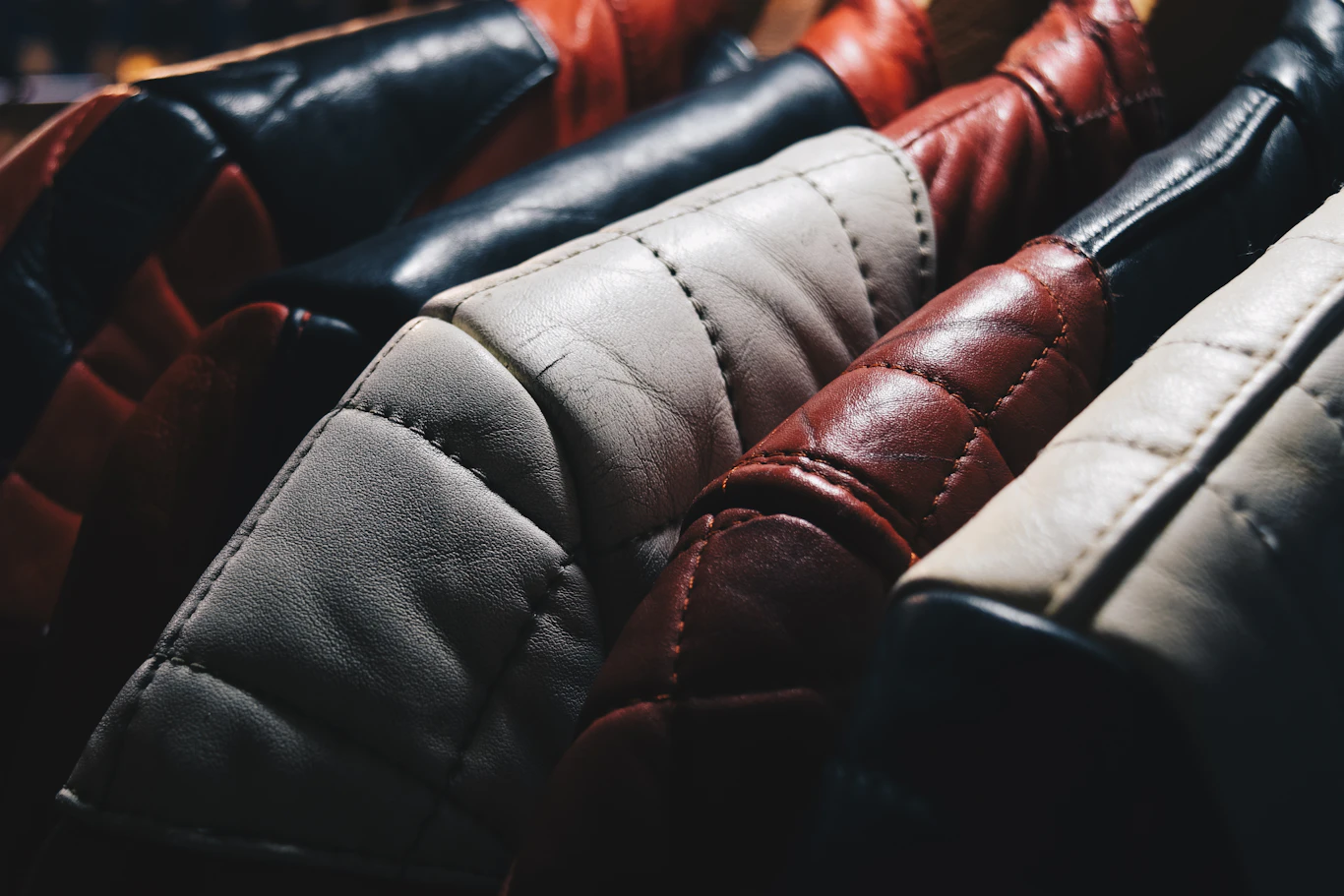 A row of finished leather jackets, quilted and stitched, in graduated tan, grey, and burgundy hides
