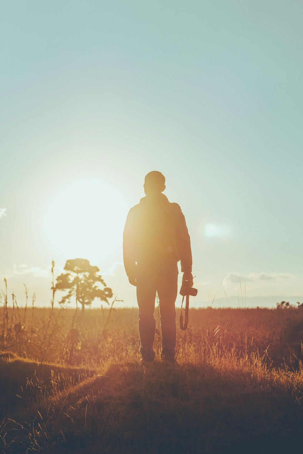 man standing on dried grass holding camera during golden hour