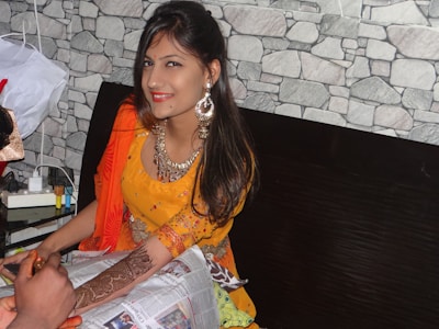 A smiling woman applying henna designs on her hands in a cozy, sunlit room.