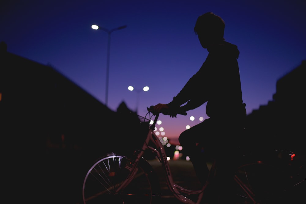 silhouette persona che cavalca in bicicletta di notte