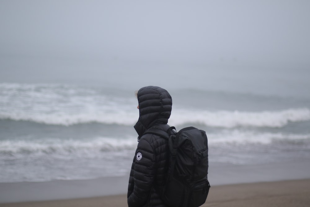 person wearing black duffle coat facing body of water