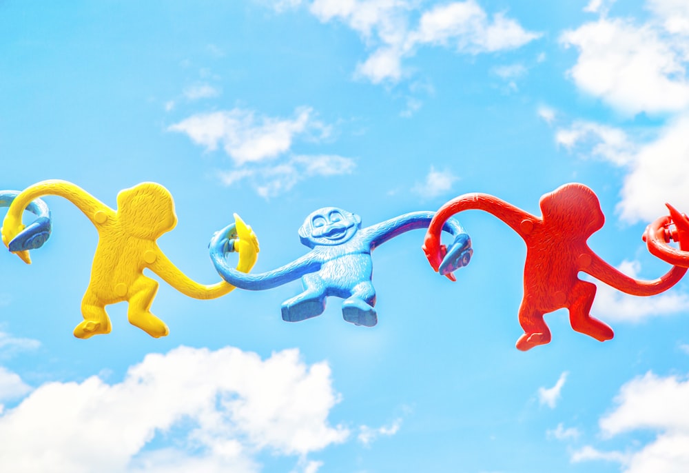 three assorted-color monkey plastic toys holding each other during daytime