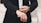 A person is adjusting the cuff of a tailored black suit jacket, wearing a white shirt underneath. The hands, adorned with a watch and a ring, are meticulously focused on the task, exuding a sense of elegance and sophistication.
