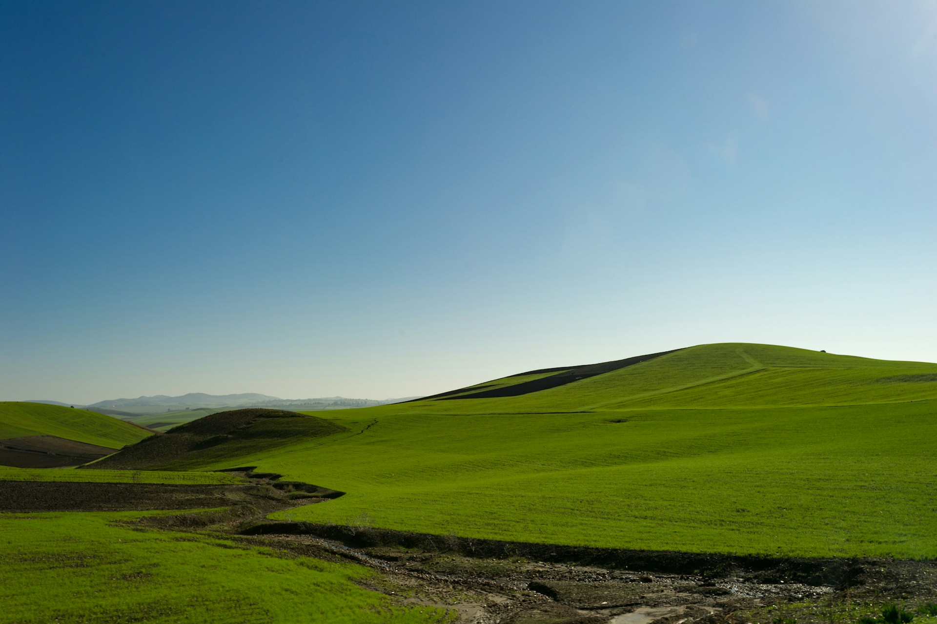 A serene landscape painting depicting rolling hills under a clear blue sky.