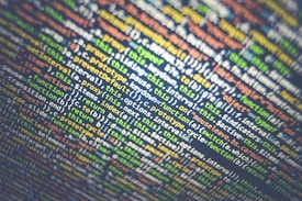 A close-up view of a computer screen filled with lines of colored text, representing programming code. The text includes various functions, variables, and syntax elements typical of a scripting or programming language.