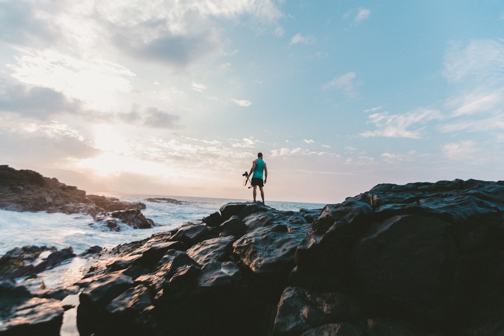 man standing on rocky shore under cloudy sky