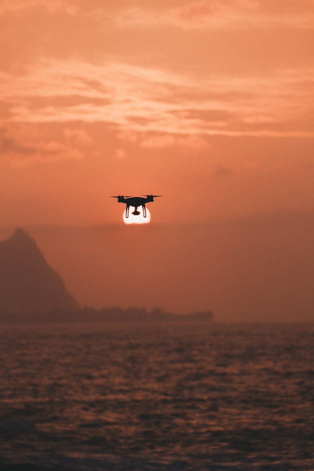 silhouette of drone hovering above body of water