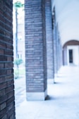 A perspective view of a corridor with brown brick columns on the left side. The floor and ceiling are smooth and white, creating a sense of depth as the hallway extends into the distance.