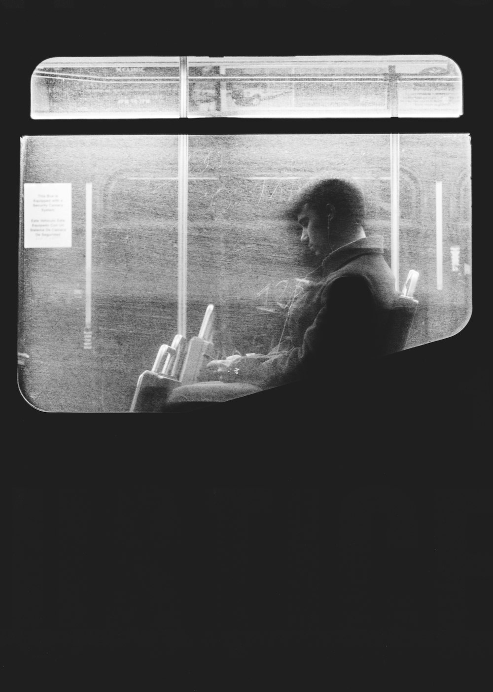 Black and white shot of man sitting on night bus through dirty window in Boston