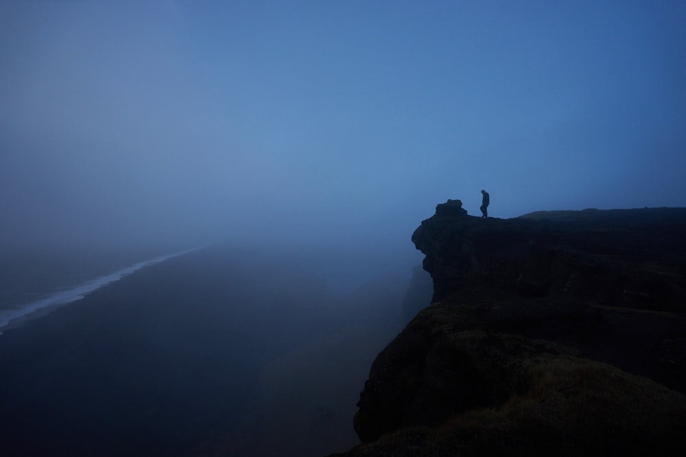 Persona de pie acantilado de roca cubierto de niebla