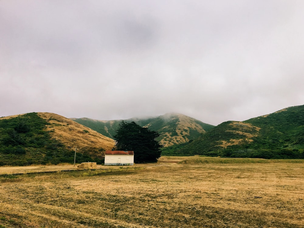 house in the middle of the field surrounded by mountains