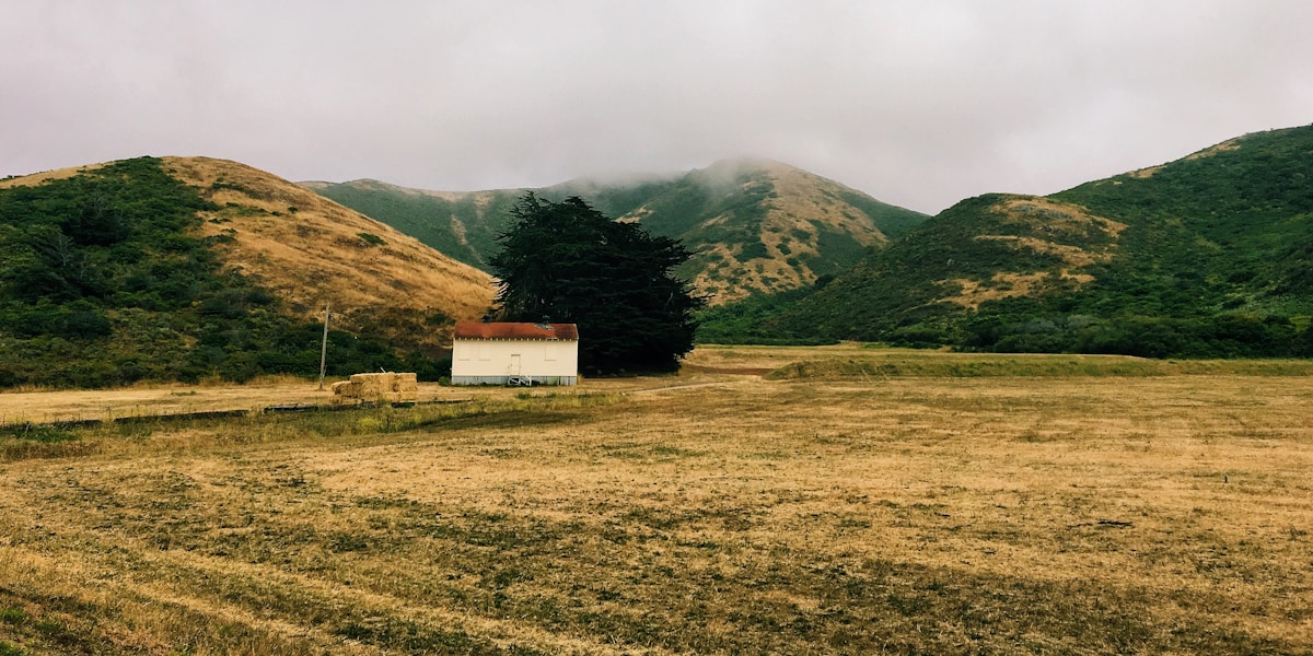 house in the middle of the field surrounded by mountains