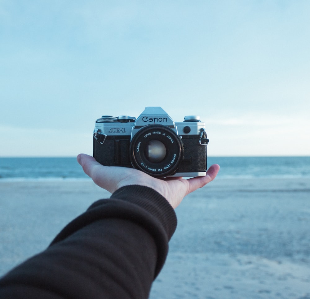 person holding black and gray Canon AE-1 bridge camera