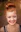 A smiling woman with red hair in a bun and visible freckles