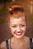 A smiling woman with red hair in a bun and visible freckles