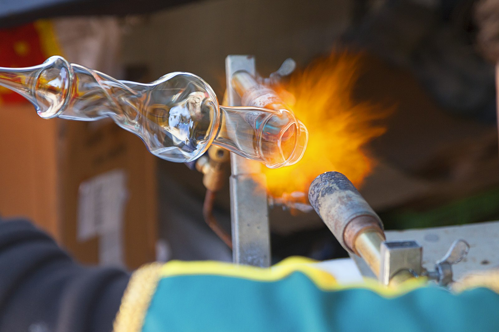 Hands shaping a glowing glass vessel with jacks at the bench