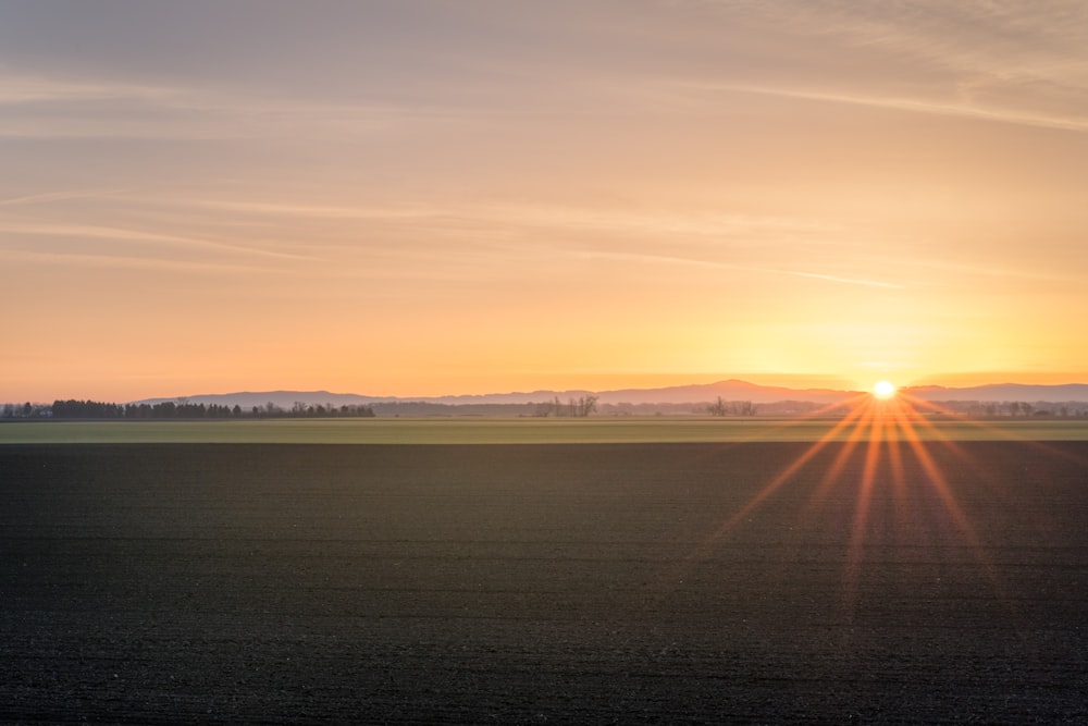 braunes Erdfeld auf der anderen Seite des Berges unter orangefarbenem Sonnenuntergangshimmel