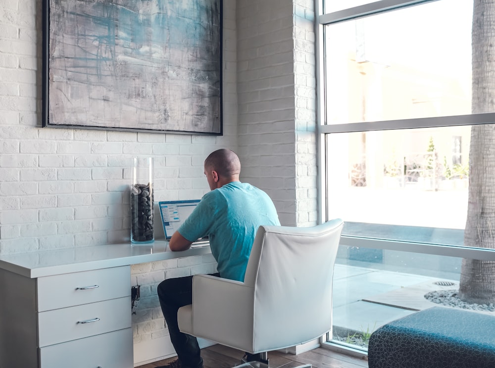 man sitting on armchair using laptop computer