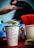 A white paper cup filled with dollar bills is prominently displayed. The cup has a handwritten message that reads, 'Tipping is not just for cows anymore.' In the background, there’s a red container with straws and a blurred figure of a person.