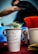 A white paper cup filled with dollar bills is prominently displayed. The cup has a handwritten message that reads, 'Tipping is not just for cows anymore.' In the background, there’s a red container with straws and a blurred figure of a person.