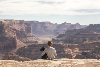 person with dog sitting on Grand Canyon cliff