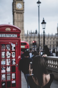 selective focus of woman taking pictures in front of red payphone