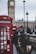 Man happily checking his phone while standing near a London street with iconic red buses.