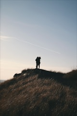 Sunset silhouette of newlyweds holding hands on a hilltop.