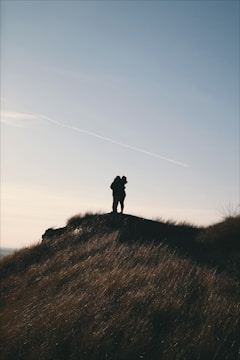 Sunset silhouette of newlyweds holding hands on a hilltop.