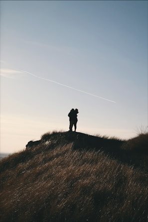 Silhouetted couple sharing a quiet moment at sunset on a hilltop.