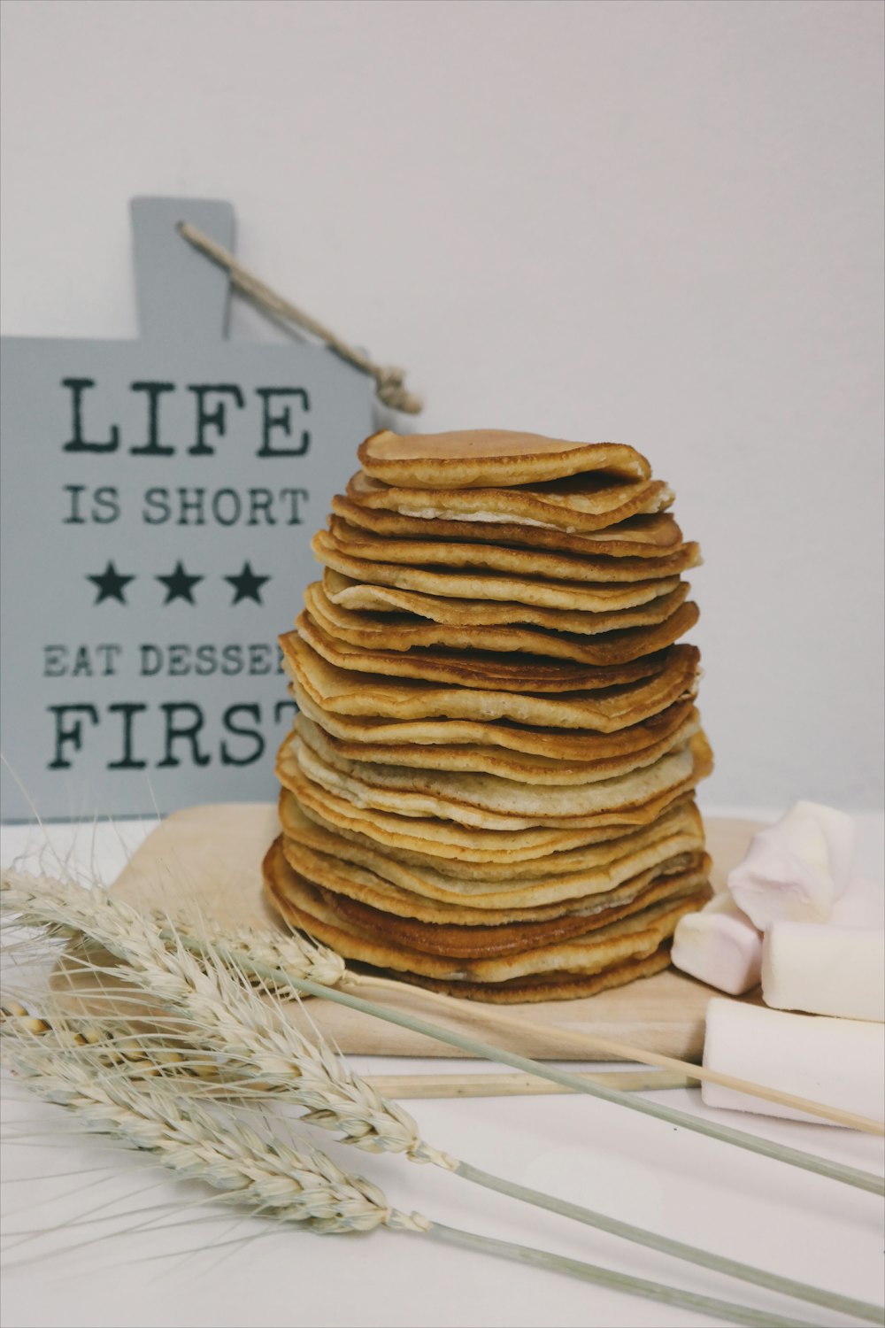 A pile of pancakes in front of a blue sign that says "Life is short - Eat pancakes first."