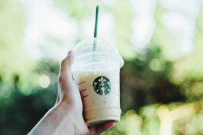 Hand holding a Twistara tumbler filled with iced coffee against a blurred outdoor background