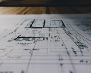 A detailed architectural blueprint spread out on a flat surface, with lines and annotations indicating various sections and measurements. The image is focused, balancing clarity with a slightly blurred background indicating depth.