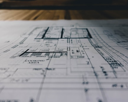 Blueprints and architectural models spread out on a table with a professional pointing at them.