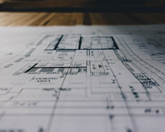 A detailed architectural blueprint spread out on a flat surface, with lines and annotations indicating various sections and measurements. The image is focused, balancing clarity with a slightly blurred background indicating depth.
