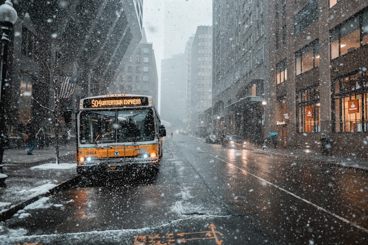 a city street in the snow with a bus and people walking on the side walk