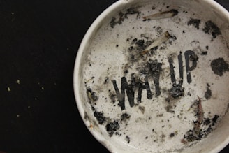 Close-up of a sleek black 3D printed urban-style ashtray with subtle white accents on a gray concrete surface.
