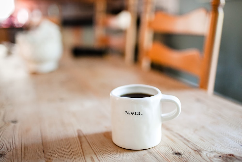 A white coffee mug with âbeginâ written on it on a wooden table