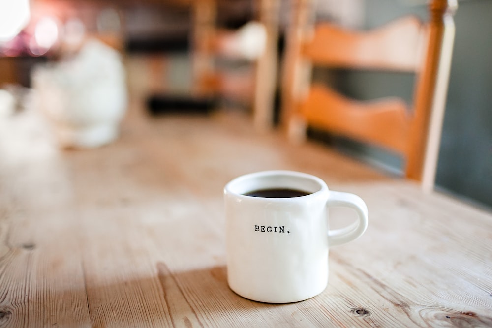 A white coffee mug with “begin” written on it on a wooden table