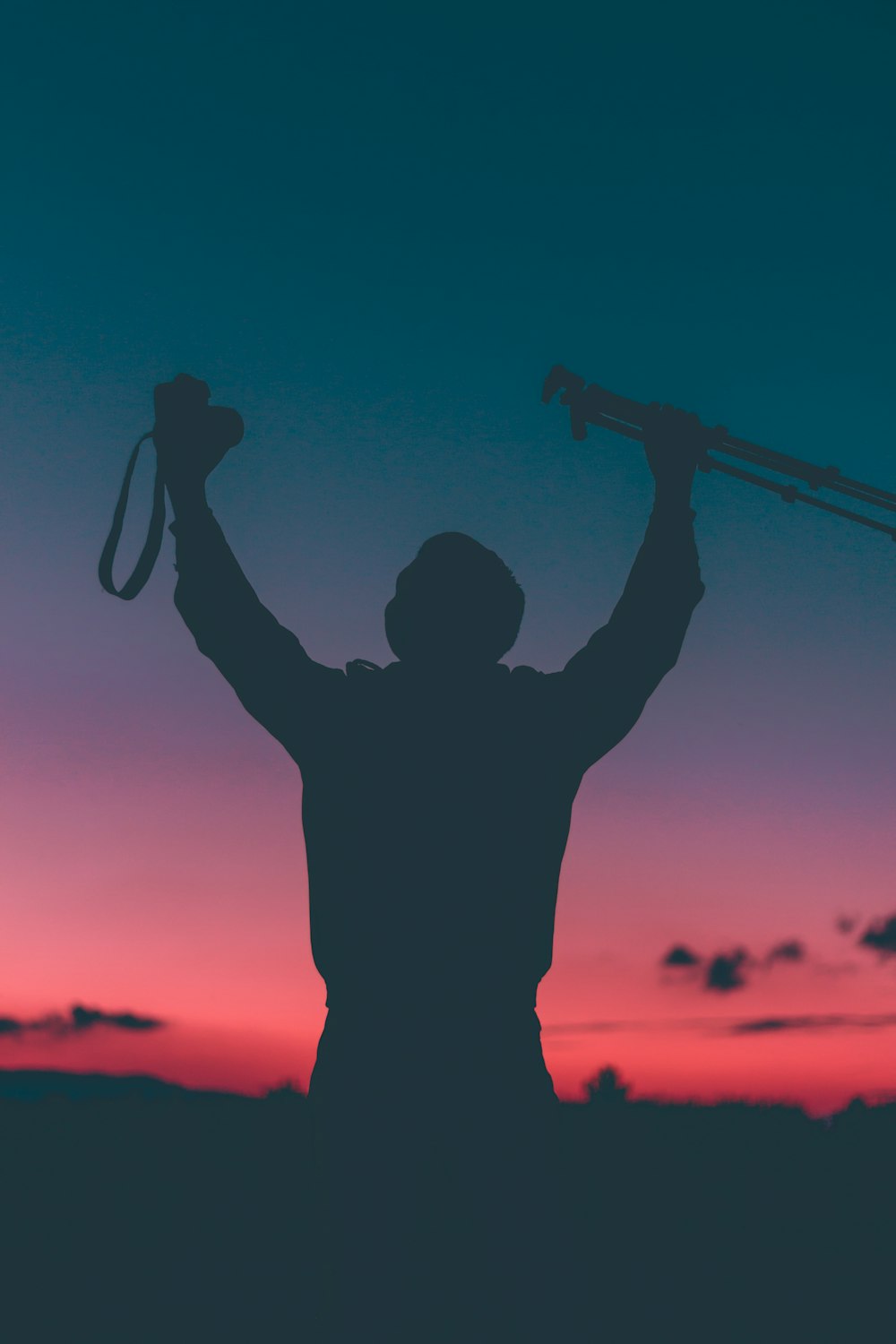 silhouette of a person raising camera and tripod with pink and blue sky