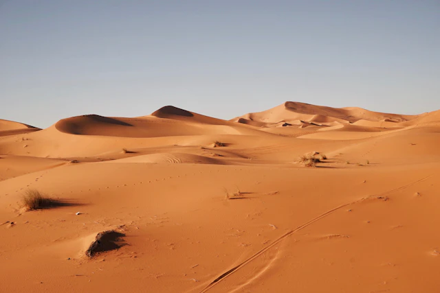 Voiture de location garée au bord d'une route goudronnée face aux dunes orangées de l'Erg Chebbi à Merzouga
